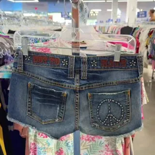 Y2K denim micro shorts with a studded peace-sign back pocket, on a hanger